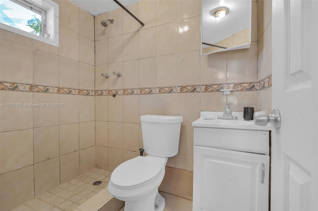 bathroom featuring vanity, toilet, tile walls, and a tile shower