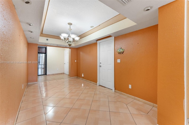 tiled empty room with a tray ceiling and a chandelier