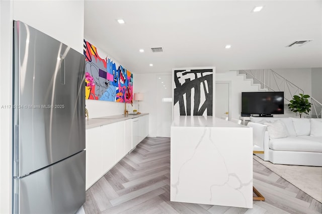 kitchen featuring stainless steel fridge, light parquet floors, white cabinetry, light stone counters, and a kitchen island