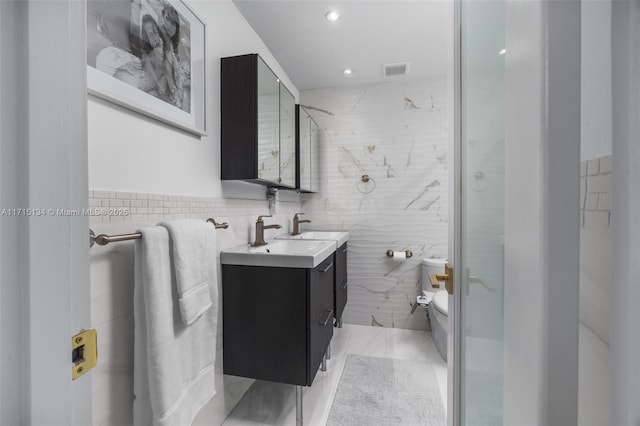 bathroom featuring vanity, toilet, a shower with shower door, and tile walls