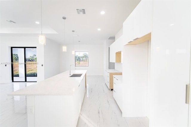 kitchen featuring hanging light fixtures, sink, white cabinets, and a center island with sink