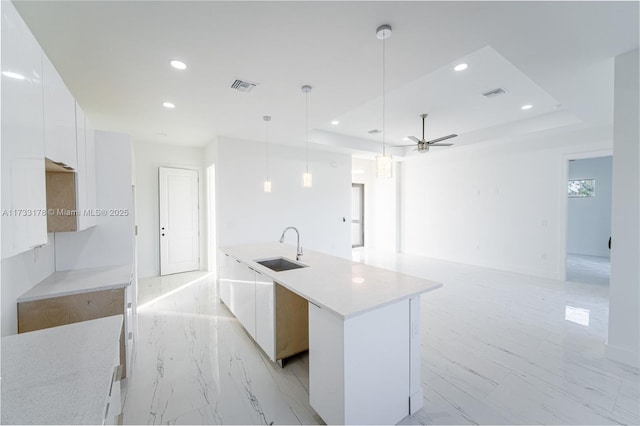 kitchen featuring sink, a raised ceiling, an island with sink, and white cabinets