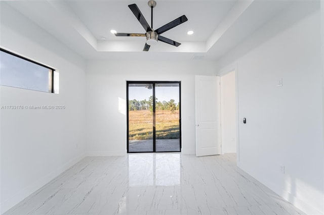 empty room with ceiling fan and a raised ceiling