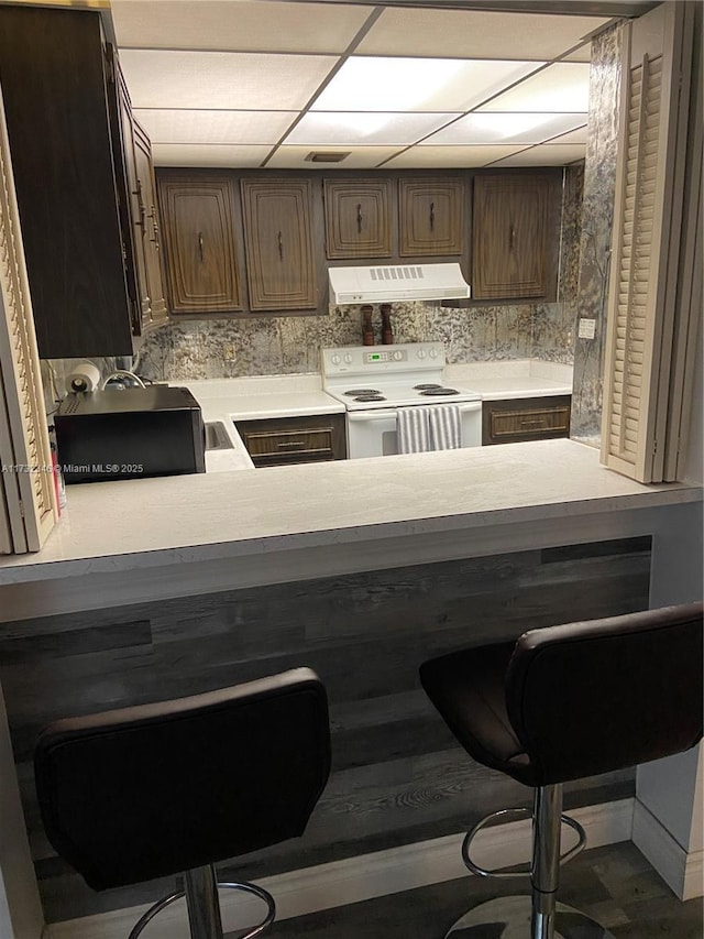 kitchen featuring white electric range, ventilation hood, a paneled ceiling, and a kitchen bar