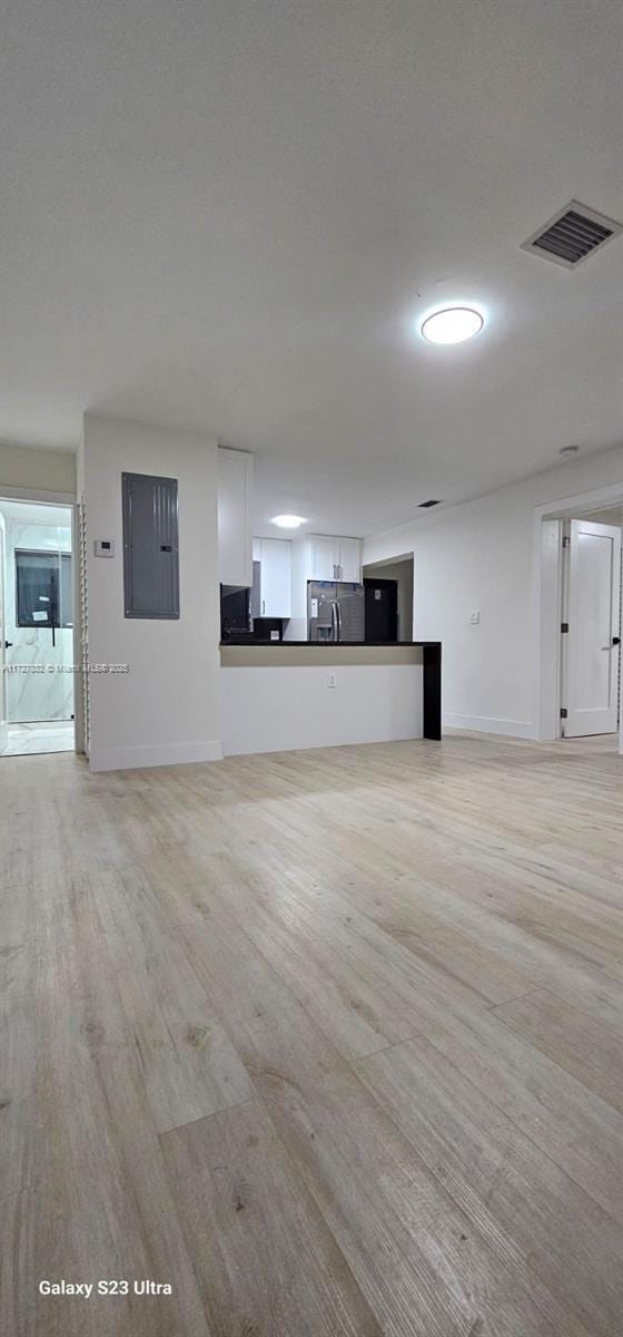 unfurnished living room featuring electric panel and light hardwood / wood-style flooring