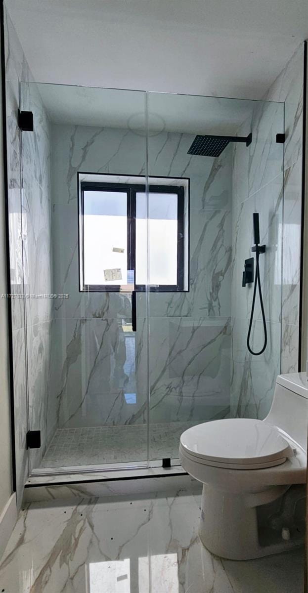 bathroom featuring a shower with shower door, toilet, and a healthy amount of sunlight