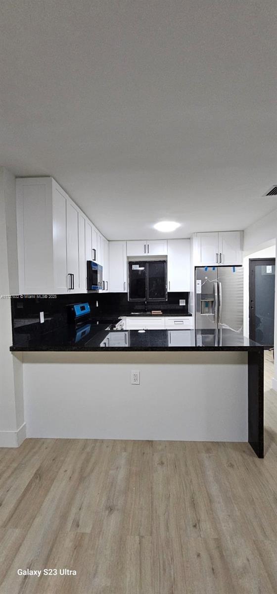 kitchen with white cabinetry, light hardwood / wood-style floors, kitchen peninsula, stainless steel appliances, and a textured ceiling