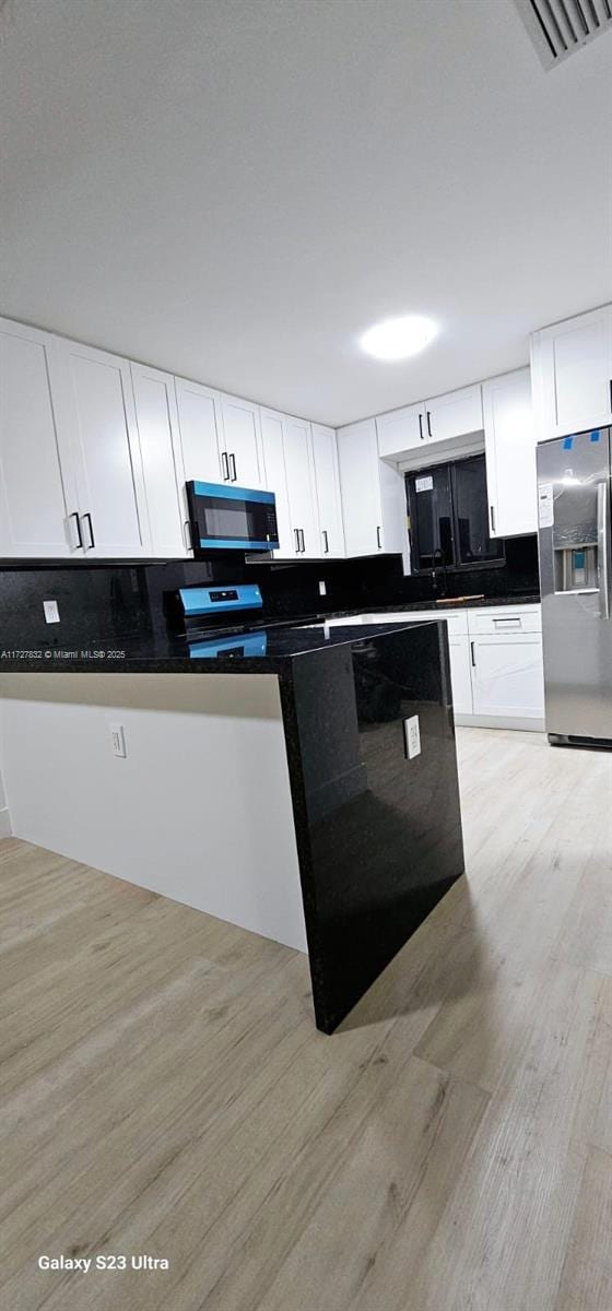 kitchen with white cabinetry, stainless steel appliances, light hardwood / wood-style floors, and decorative backsplash