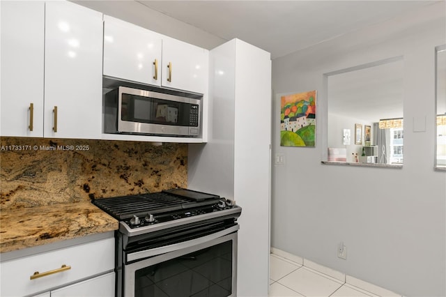 kitchen featuring appliances with stainless steel finishes, stone countertops, white cabinets, backsplash, and light tile patterned floors