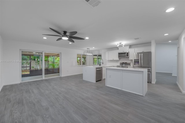 kitchen featuring hardwood / wood-style flooring, appliances with stainless steel finishes, white cabinets, decorative light fixtures, and kitchen peninsula