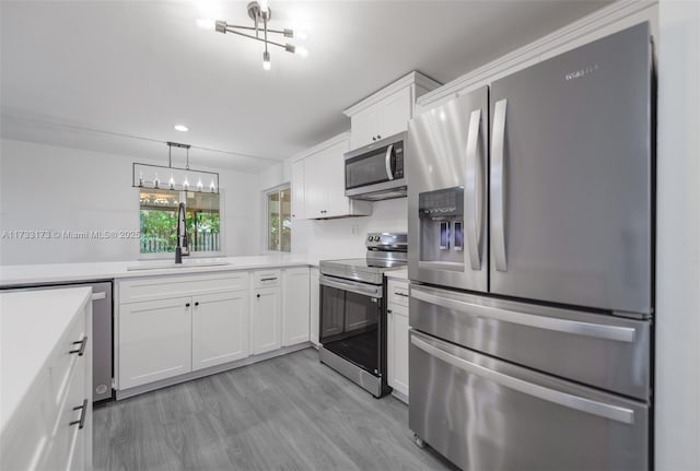 kitchen featuring appliances with stainless steel finishes, white cabinetry, sink, hanging light fixtures, and light hardwood / wood-style floors