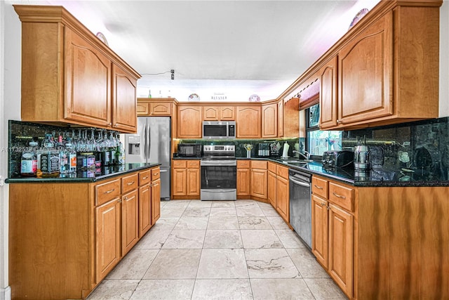 kitchen featuring stainless steel appliances, sink, decorative backsplash, and dark stone countertops