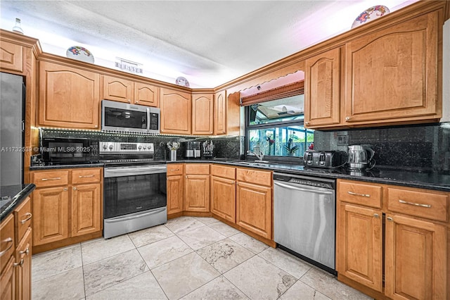 kitchen featuring sink, decorative backsplash, stainless steel appliances, and dark stone counters