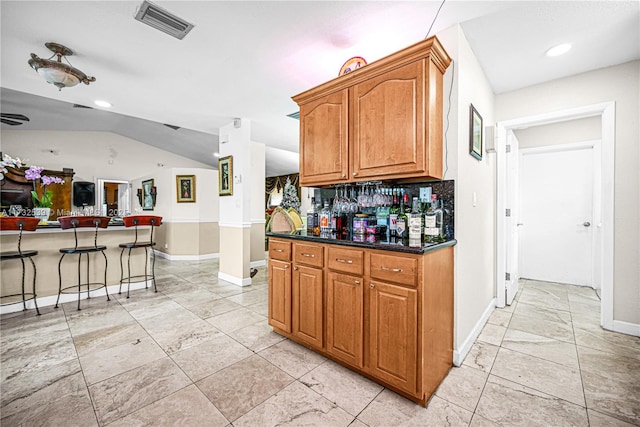510 NW 105th Dr, Coral Springs, FL 33071 - kitchen featuring dark countertops, visible vents, brown cabinets, a breakfast bar area, and lofted ceiling