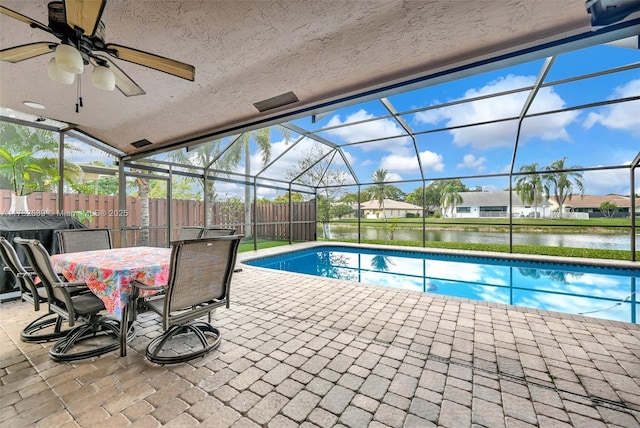 view of pool featuring glass enclosure, a patio, ceiling fan, and a water view