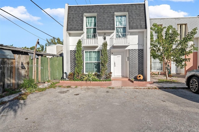 view of front facade featuring mansard roof, fence, stucco siding, and a shingled roof