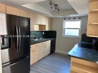 kitchen featuring dark countertops, a sink, a raised ceiling, backsplash, and black refrigerator with ice dispenser