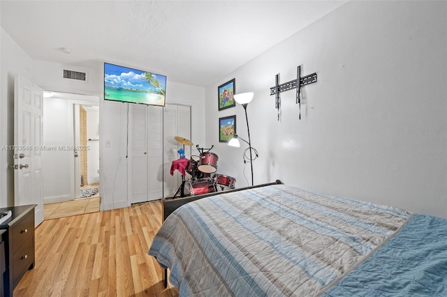 bedroom with light wood finished floors, visible vents, and a closet