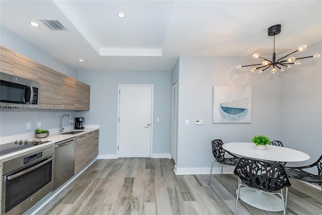 kitchen featuring stainless steel appliances, sink, light wood-type flooring, and a tray ceiling