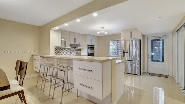 kitchen with a breakfast bar, stainless steel appliances, white cabinets, decorative backsplash, and kitchen peninsula