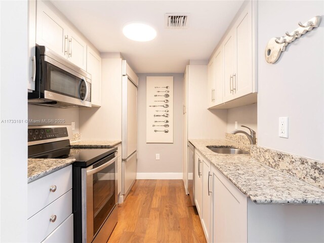 kitchen with sink, white cabinets, light hardwood / wood-style floors, stainless steel appliances, and light stone countertops