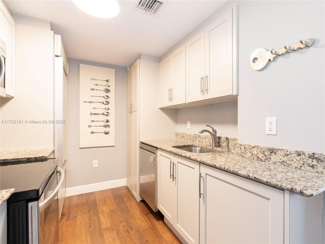 kitchen with stainless steel appliances, light stone countertops, sink, and white cabinets