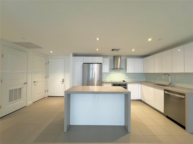 kitchen featuring a kitchen island, white cabinetry, sink, stainless steel appliances, and wall chimney exhaust hood