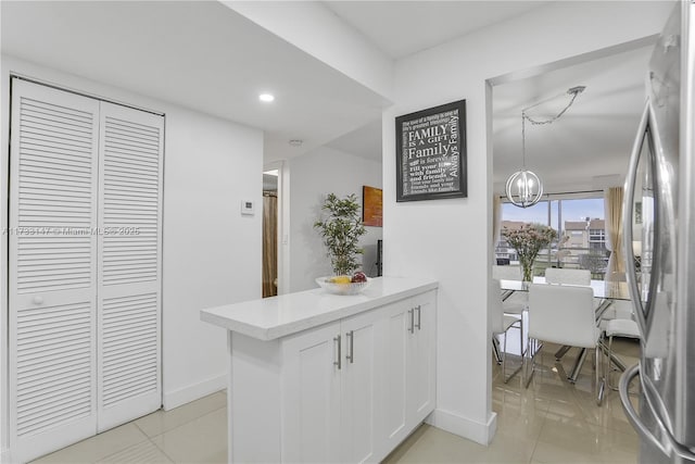 kitchen with light tile patterned flooring, stainless steel refrigerator, a notable chandelier, pendant lighting, and white cabinets