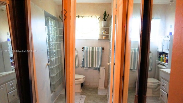 bathroom with vanity, a shower, tile walls, and toilet