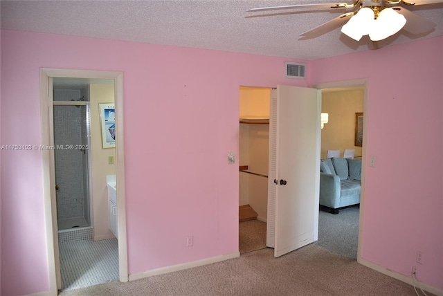 unfurnished bedroom with ensuite bathroom, light carpet, a textured ceiling, and ceiling fan