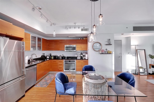 kitchen with appliances with stainless steel finishes, sink, pendant lighting, and light wood-type flooring