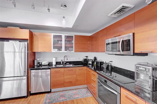 kitchen with sink, light hardwood / wood-style flooring, appliances with stainless steel finishes, dark stone countertops, and hanging light fixtures