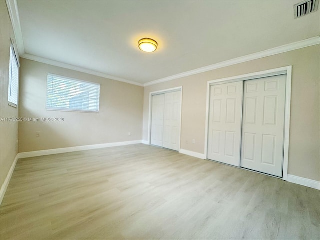 unfurnished bedroom with ornamental molding, two closets, and light hardwood / wood-style flooring