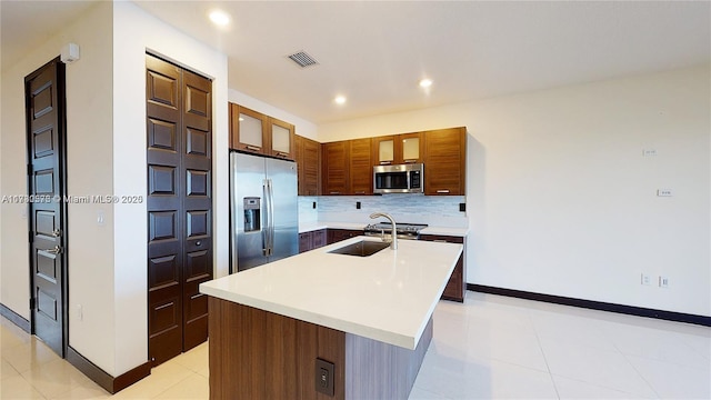 kitchen with sink, light tile patterned floors, stainless steel appliances, a center island with sink, and decorative backsplash