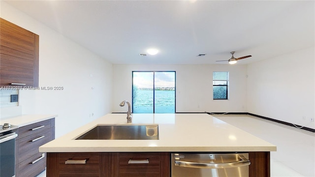 kitchen with sink, ceiling fan, stainless steel appliances, dark brown cabinets, and a center island with sink