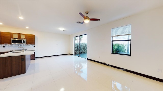 kitchen featuring sink, a center island with sink, light tile patterned floors, ceiling fan, and backsplash