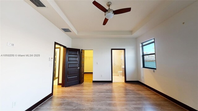 unfurnished bedroom with hardwood / wood-style flooring, ceiling fan, ensuite bathroom, a spacious closet, and a raised ceiling