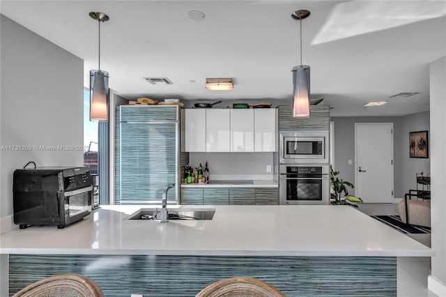 kitchen featuring appliances with stainless steel finishes, white cabinetry, sink, hanging light fixtures, and kitchen peninsula