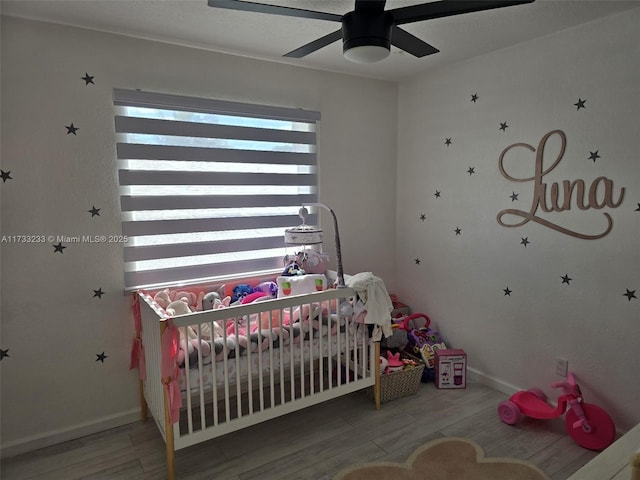 bedroom with hardwood / wood-style floors, a crib, and ceiling fan