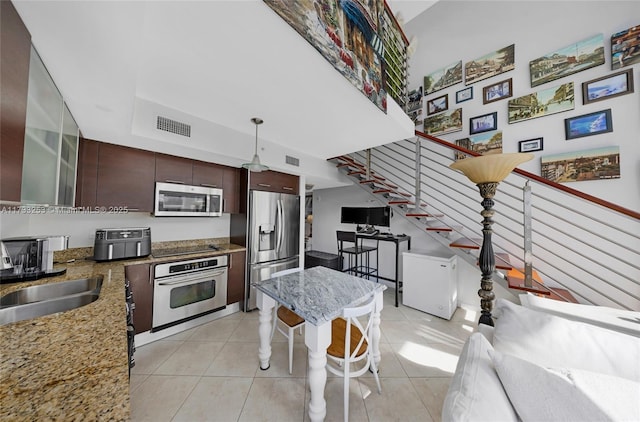 kitchen with sink, light tile patterned floors, appliances with stainless steel finishes, hanging light fixtures, and dark brown cabinets