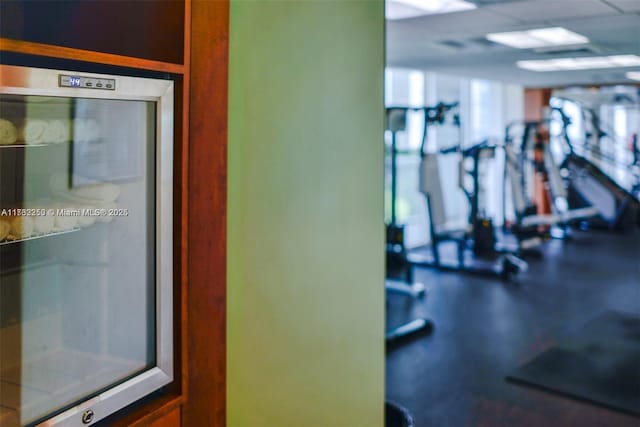 exercise room featuring beverage cooler and a drop ceiling