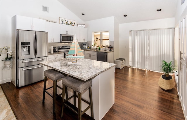 kitchen featuring appliances with stainless steel finishes, white cabinets, a kitchen breakfast bar, a center island, and light stone counters