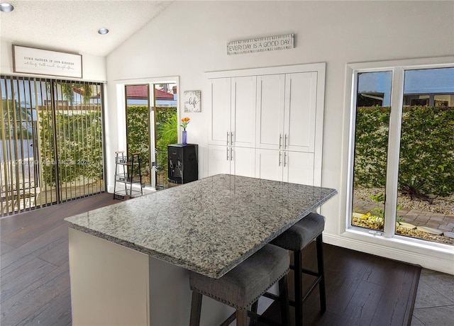 kitchen featuring dark wood-type flooring, a kitchen bar, light stone counters, white cabinetry, and vaulted ceiling