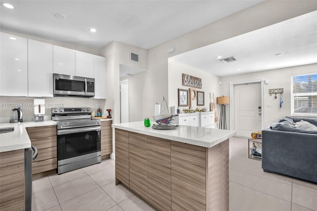 kitchen featuring a kitchen island, light tile patterned flooring, white cabinets, and appliances with stainless steel finishes