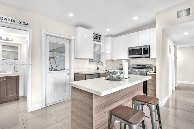 kitchen featuring a center island, light tile patterned floors, a kitchen breakfast bar, stainless steel appliances, and white cabinets