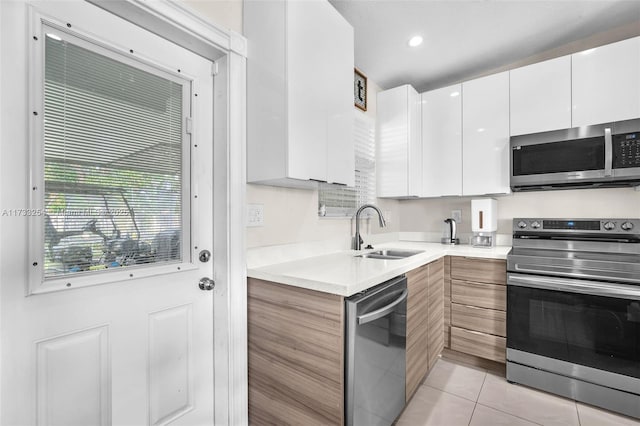 kitchen with stainless steel appliances, light tile patterned flooring, sink, and white cabinets