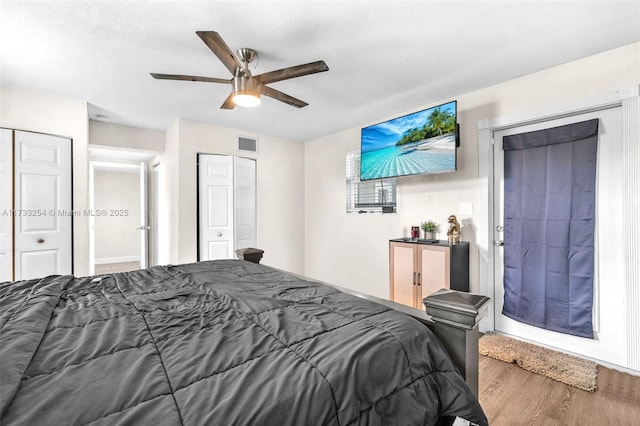 bedroom with ceiling fan, a textured ceiling, wood-type flooring, and multiple closets