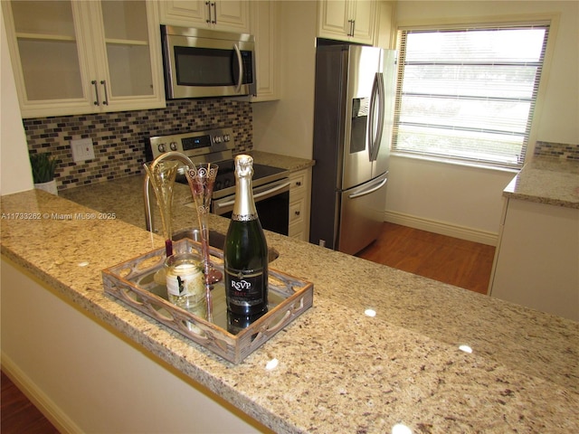 kitchen with decorative backsplash, light stone countertops, hardwood / wood-style flooring, and appliances with stainless steel finishes