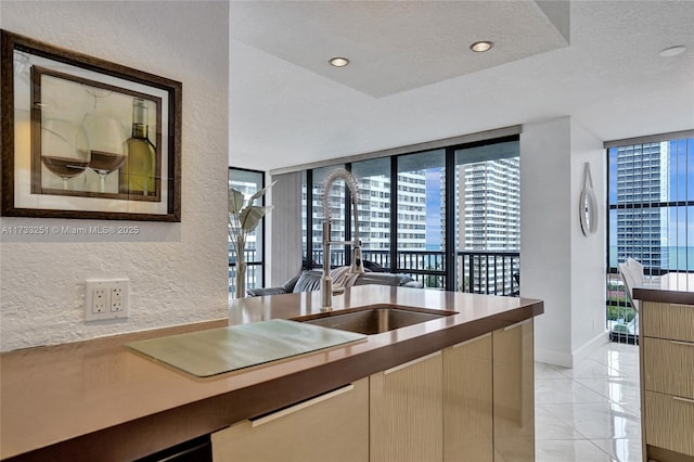 kitchen featuring sink, light tile patterned floors, a textured ceiling, and a wall of windows