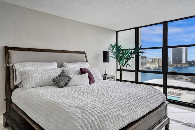 tiled bedroom featuring a water view, a textured ceiling, and a wall of windows